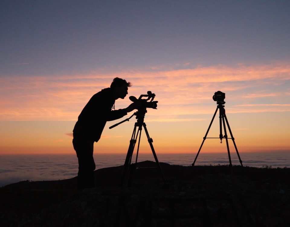 silhouette photo of person holding camera on tripod stand outside